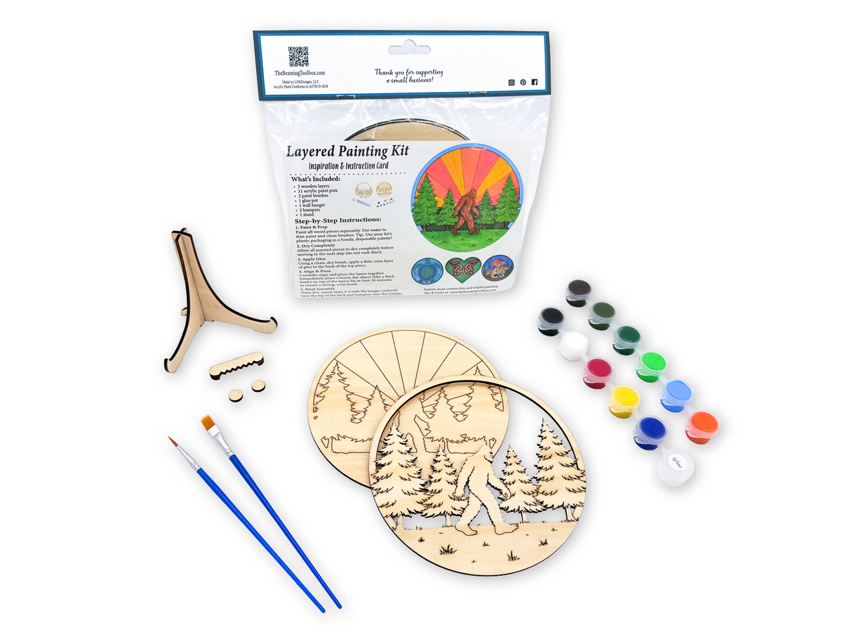Complete Sasquatch adult craft kit with packaged kit, unpainted wood layers, paints, brushes, and display hardware on a white background.