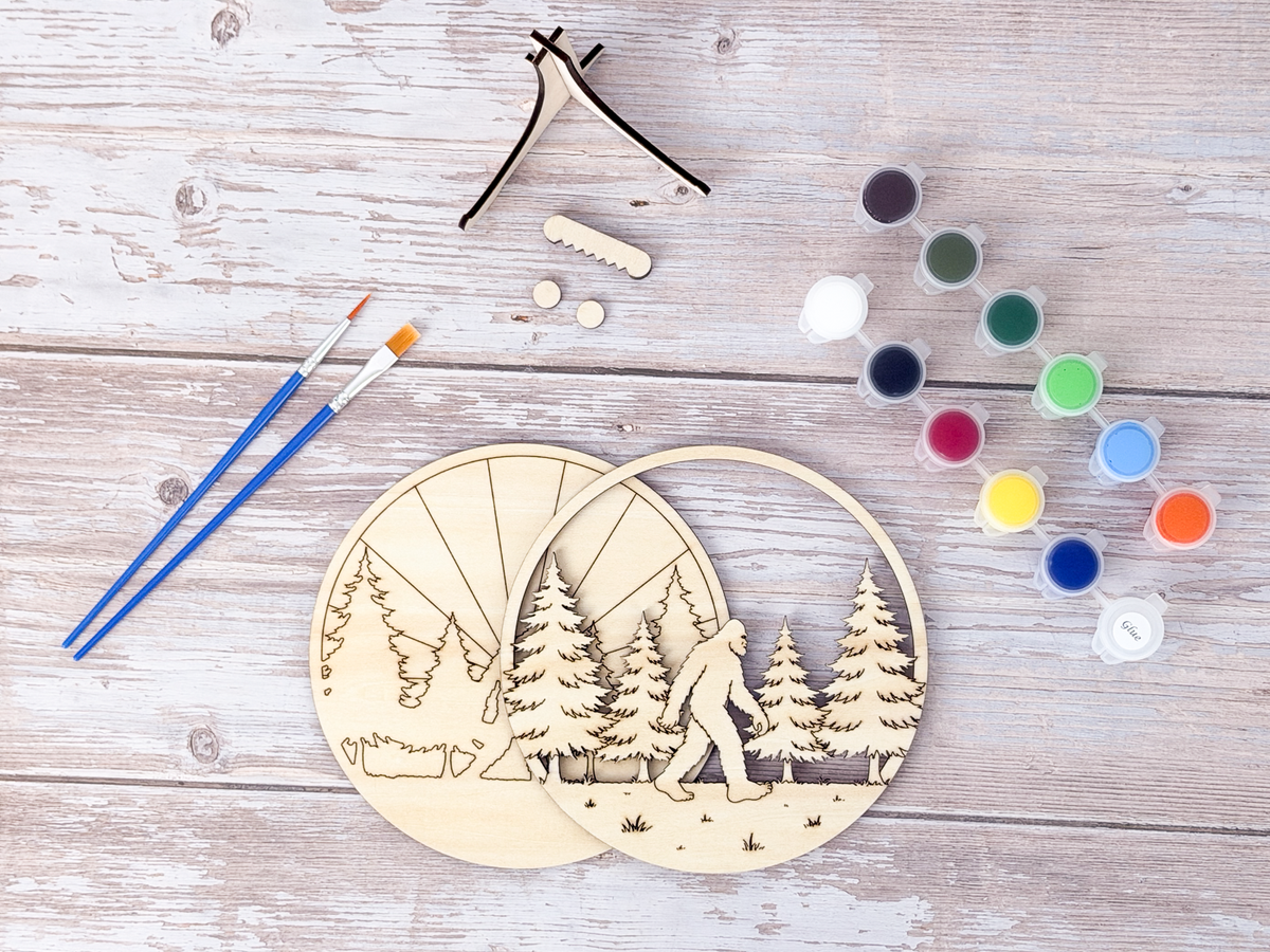 Sasquatch adult craft kit wood layers arranged with paints, brushes, stand pieces, and display hardware before painting.