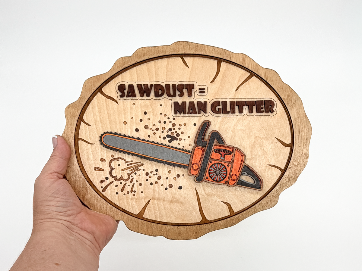 Hand holding Sawdust = Man Glitter layered wood wall art with an orange chainsaw design to show the finished size.
