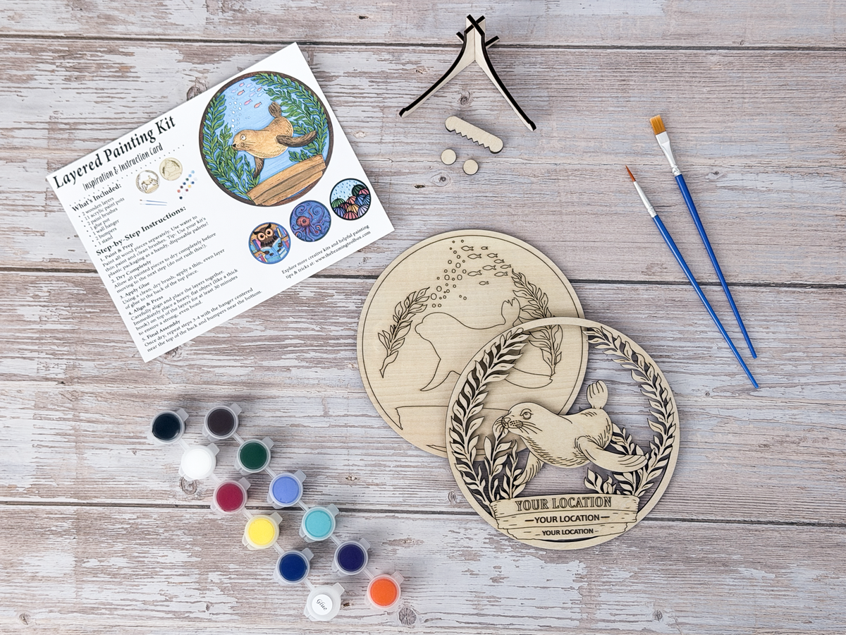 Sea Lion custom location DIY wood painting kit with unfinished layers, paint pots, brushes, display stand, packaging, and finished example.