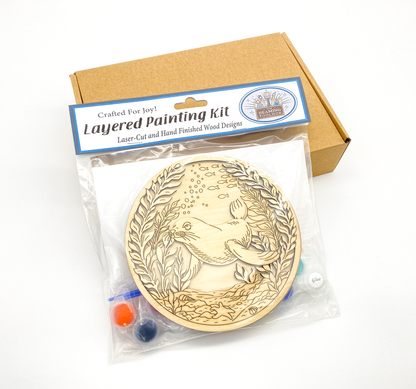 Sea lion DIY paint kit packaged in clear bag with label, showing layered wood pieces, paint pots and brushes inside