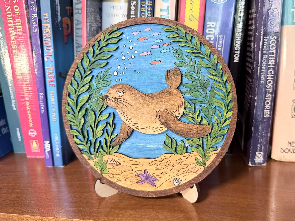 Finished Sea Lion layered wood artwork painted with a swimming sea lion, kelp, fish, bubbles, blue water, and sandy ocean floor.