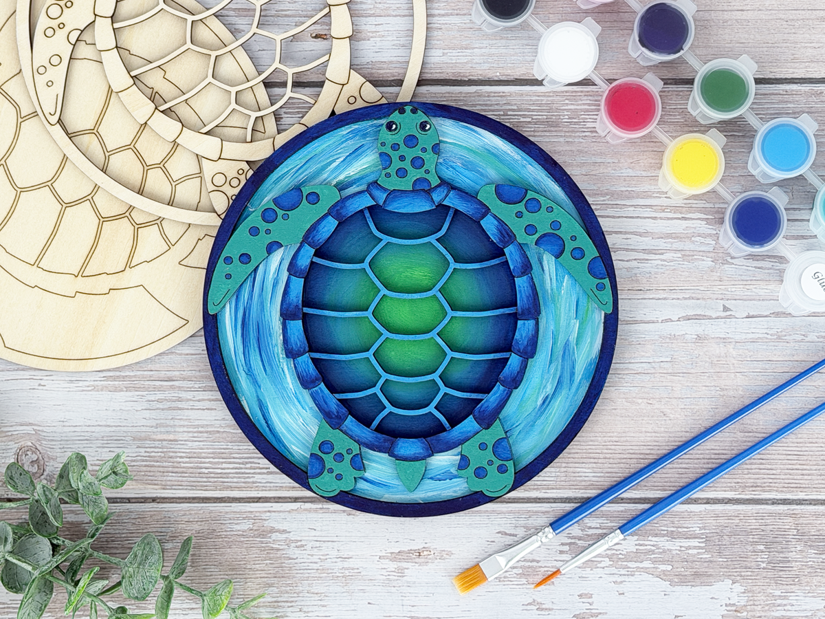 Finished sea turtle adult craft kit shown with painted layered wood artwork, unpainted kit pieces, paint pots, and brushes on a rustic wood background.