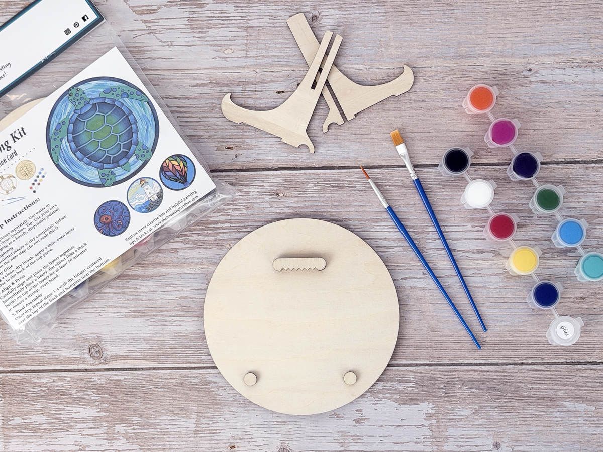 Sea turtle adult craft kit supplies with paint pots, brushes, wood display stand pieces, packaged kit, and round wood backing.
