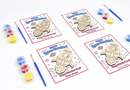 Four Valentine's Day cards with space-themed designs and coloring supplies on a white background.