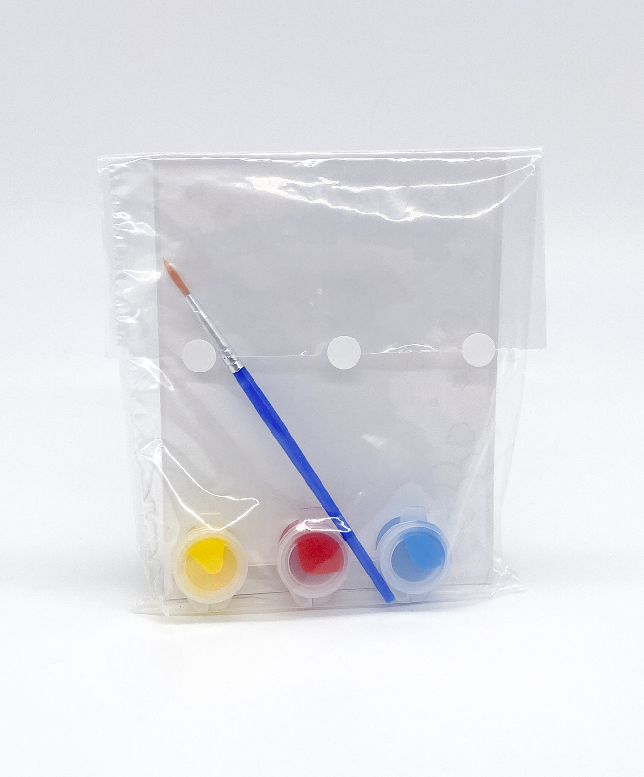 Set of paintbrushes and small containers of paint in a clear plastic bag on a white background