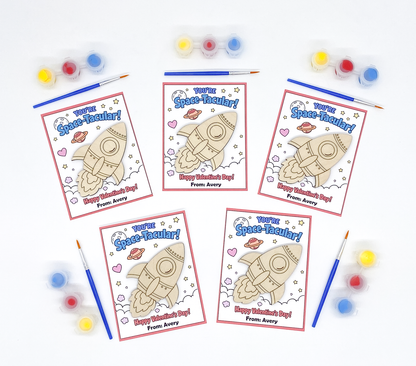 Five 'Space-Tacular' themed coloring pages with space-themed designs and text, surrounded by paint bottles and brushes on a white background.