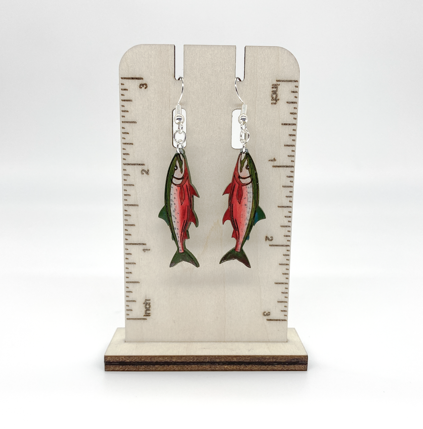 Salmon-shaped earrings on a wooden stand with measurement markings.