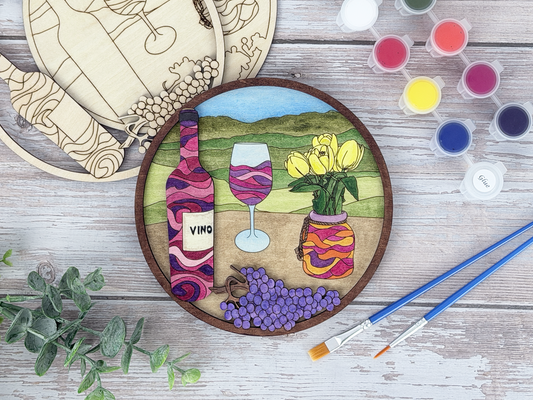 Finished wine and tulips adult craft kit shown with painted layered wood artwork, unpainted kit pieces, paint pots, and brushes on a rustic wood background.