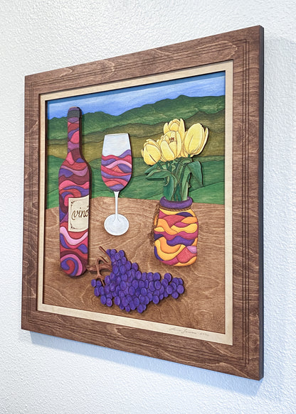 Decorative wall art with wine bottle, glass, and flowers in a wooden frame.