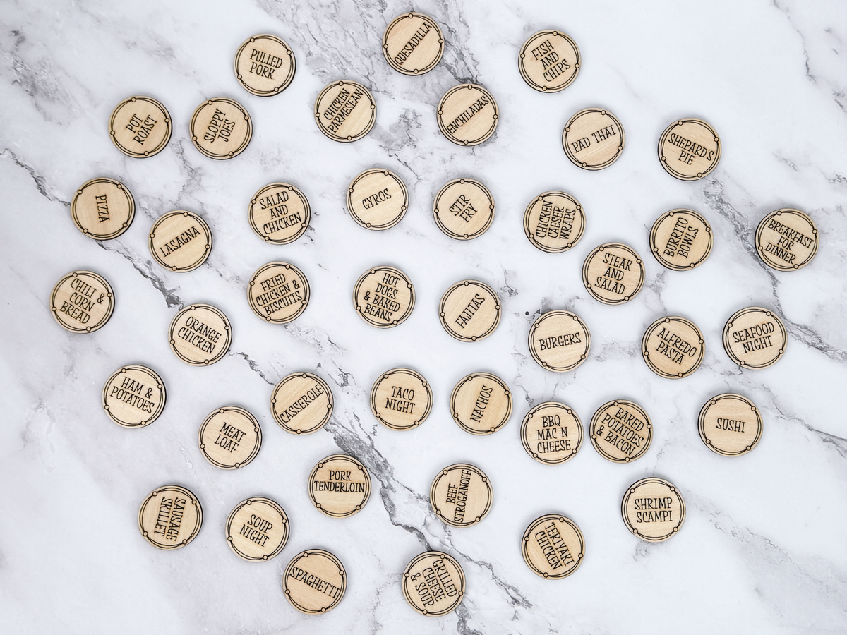 A collection of round, laser-cut wood tokens or pucks scattered on a white and gray marble surface. Each wood token is engraved with a different food category or restaurant item such as 'Pizza', 'Burgers', 'Sushi', 'Tacos', 'Pizza Pizza', and 'Baked Potato'.