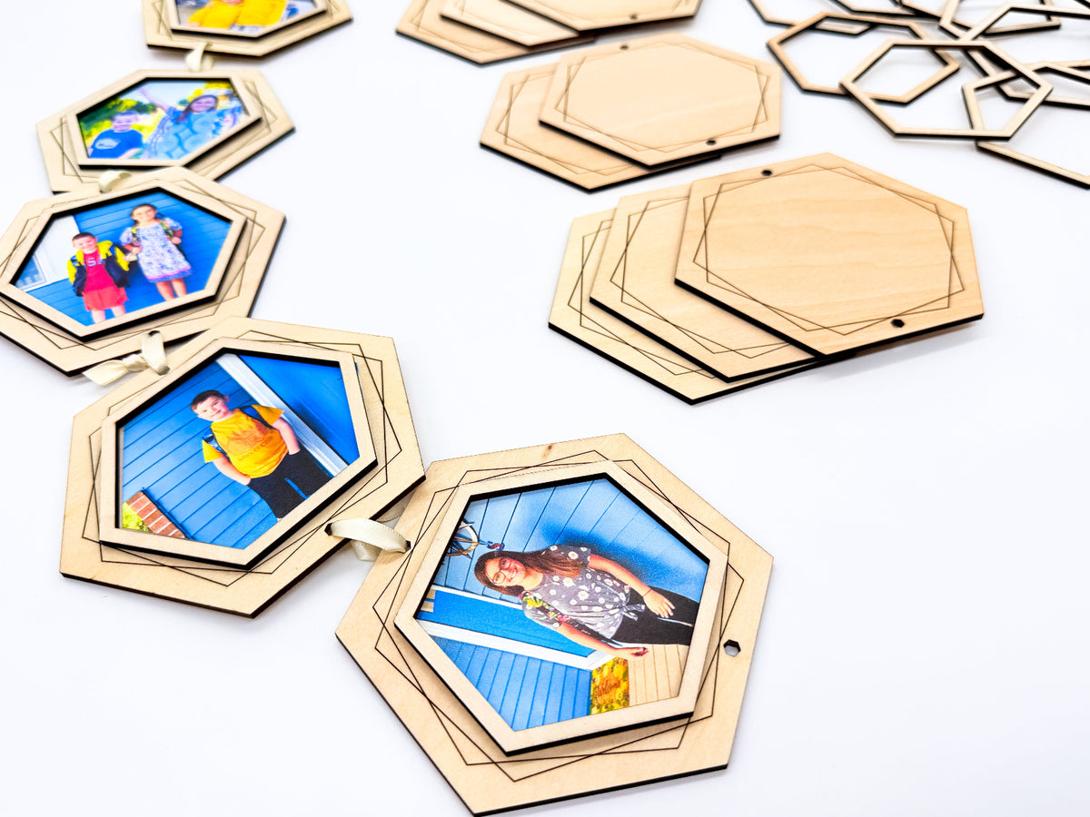 Close-up of light wooden hexagon photo frames connected with cream ribbon, alongside engraved wooden backings and separate open frame pieces.