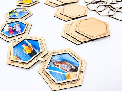 Close-up of light wooden hexagon photo frames connected with cream ribbon, alongside engraved wooden backings and separate open frame pieces.