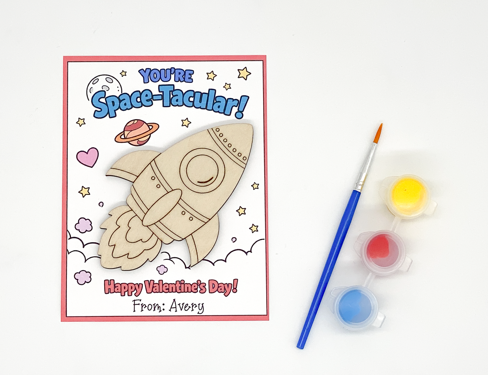 Space-themed Valentine's Day card with a wooden rocket, paintbrush, and paint on a white background